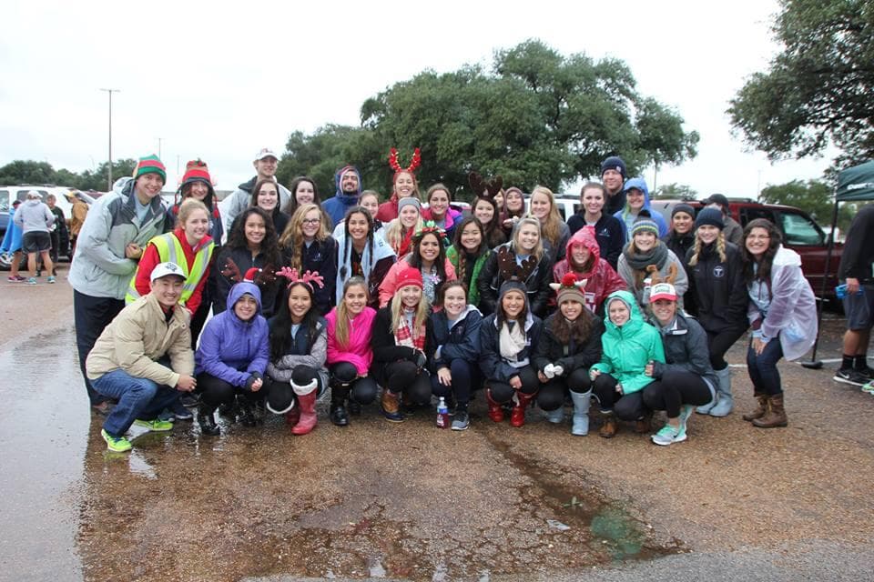 Large group photo of participants at the First Annual Prancing for Prosthetics event, wearing winter gear and holiday accessories on a rainy day