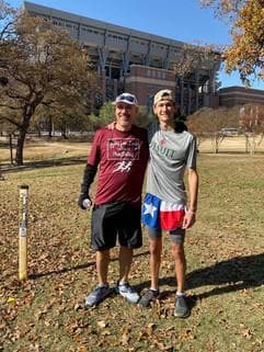 Two participants posing together near a campus building, one in maroon shirt and one in Texas flag shorts