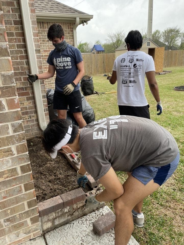 AFL members wearing masks and gloves doing landscaping work around a brick house during The Big Event 2021
