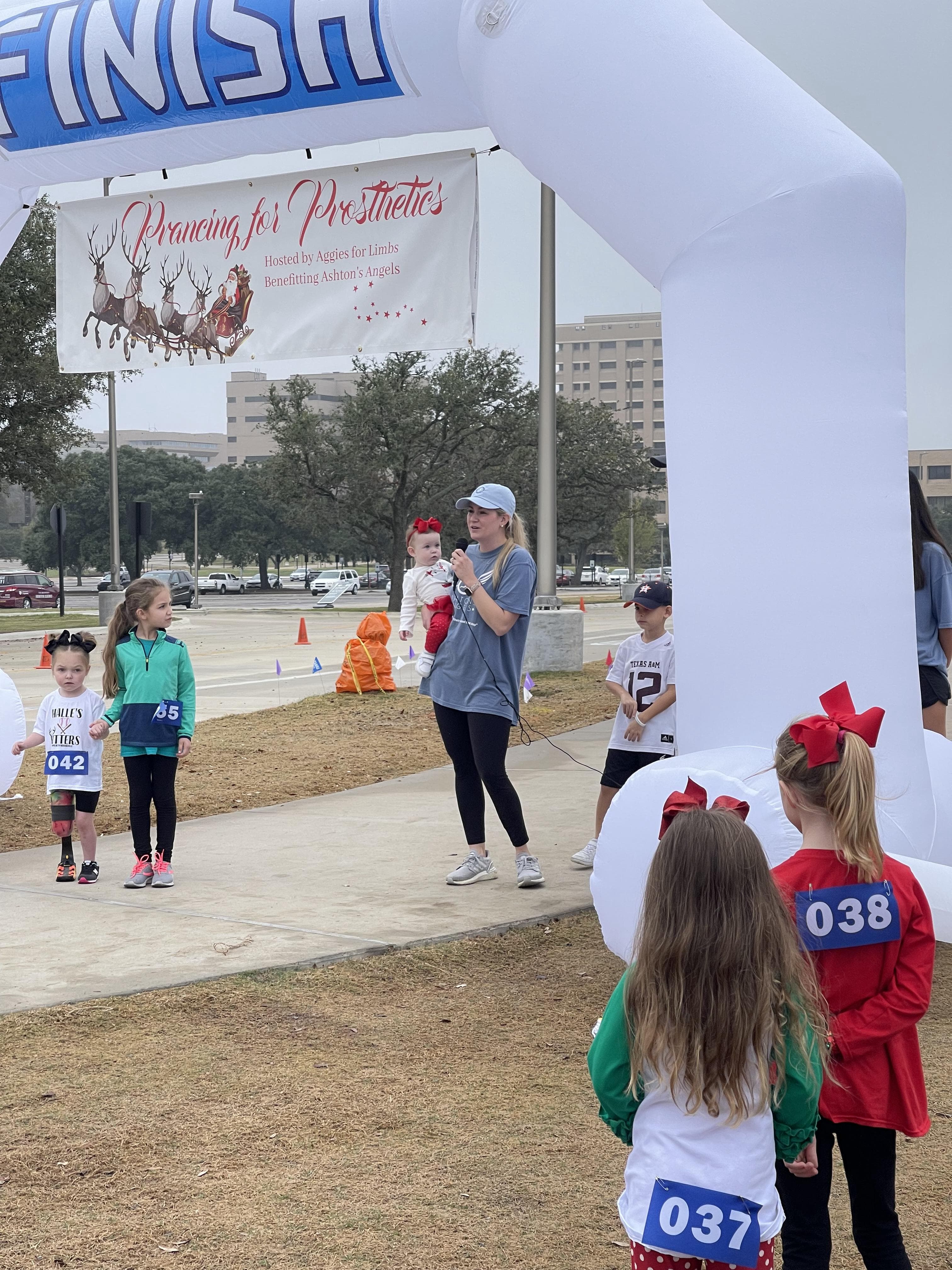 Race finish line with Prancing for Prosthetics banner and inflatable arch, showing young participants with race numbers