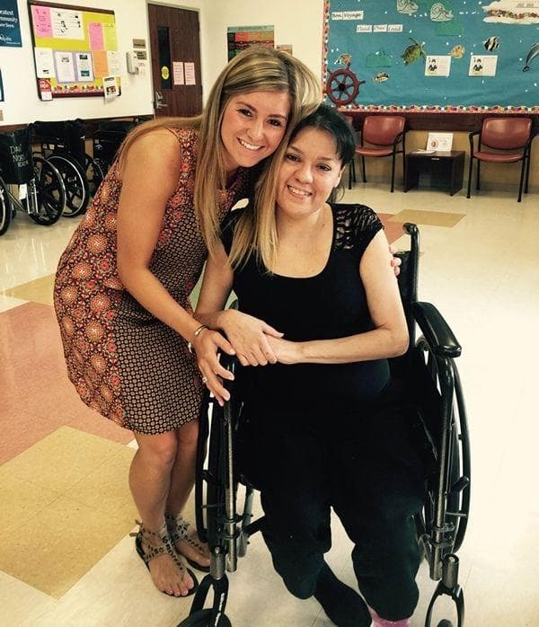 An Aggies for Limbs member sharing a warm moment with a person in a wheelchair, both smiling brightly in an indoor setting